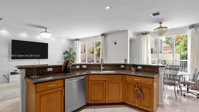 kitchen with an inviting chandelier, stainless steel dishwasher, dark stone counters, and sink