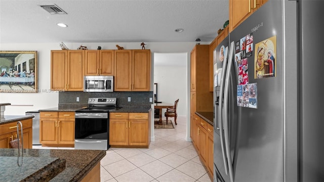 kitchen with decorative backsplash, dark stone countertops, a textured ceiling, light tile patterned flooring, and stainless steel appliances