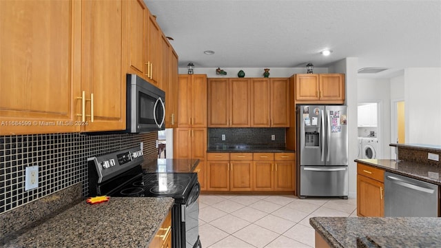 kitchen with stainless steel appliances, backsplash, dark stone countertops, washer / clothes dryer, and light tile patterned flooring