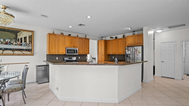 kitchen with appliances with stainless steel finishes, tasteful backsplash, light tile patterned floors, and a kitchen island with sink