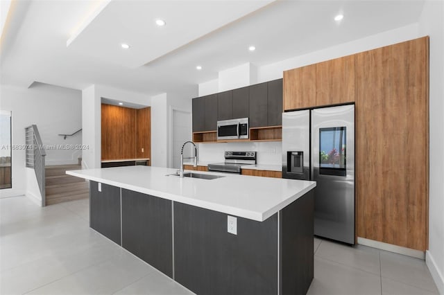 kitchen featuring a center island with sink, light tile patterned flooring, sink, and appliances with stainless steel finishes