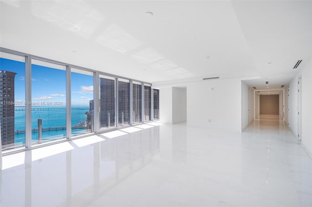 empty room with expansive windows, a water view, and light tile patterned floors