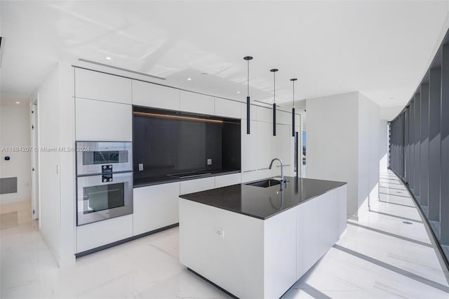 kitchen with a large island with sink, sink, stainless steel double oven, white cabinetry, and decorative light fixtures