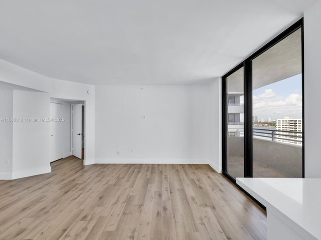 empty room featuring baseboards, floor to ceiling windows, and light wood-style floors