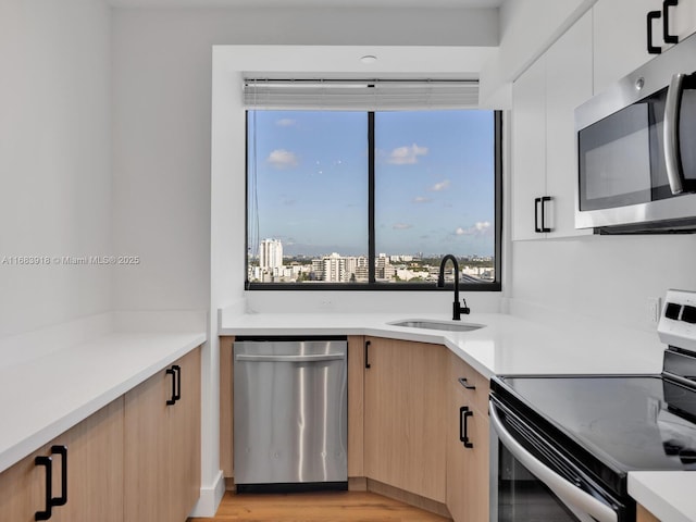 kitchen with light brown cabinets, a sink, modern cabinets, light countertops, and appliances with stainless steel finishes