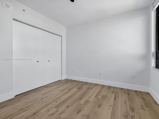 unfurnished bedroom featuring light wood finished floors, baseboards, and a closet