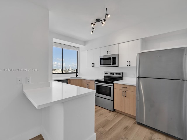 kitchen featuring a peninsula, a sink, light wood-style floors, light countertops, and appliances with stainless steel finishes