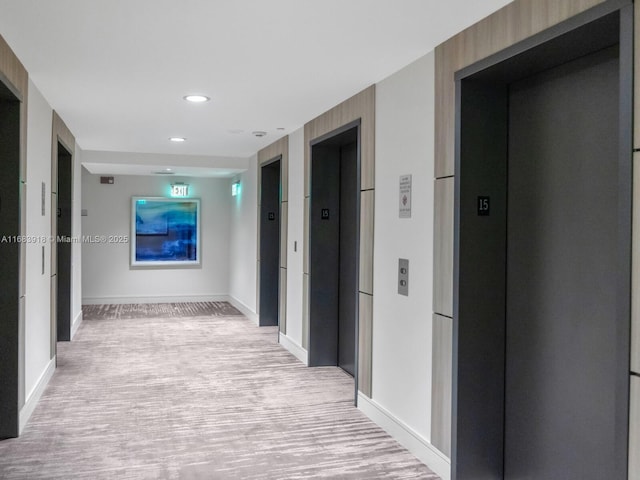 hallway featuring baseboards, light wood finished floors, recessed lighting, and elevator