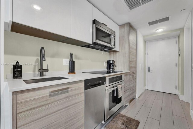 kitchen featuring stainless steel appliances, sink, white cabinets, and light wood-type flooring