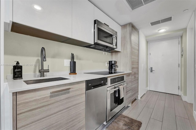 kitchen featuring appliances with stainless steel finishes, sink, white cabinets, and light hardwood / wood-style floors