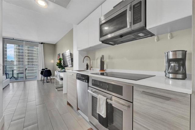 kitchen with stainless steel appliances, white cabinetry, floor to ceiling windows, and sink