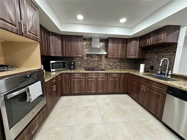 kitchen with light stone counters, appliances with stainless steel finishes, wall chimney exhaust hood, dark brown cabinetry, and sink