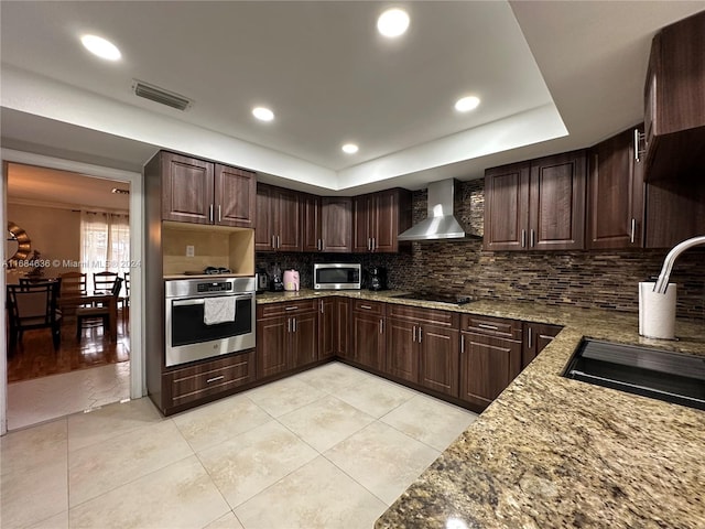 kitchen featuring sink, dark brown cabinets, stainless steel appliances, wall chimney exhaust hood, and light stone counters