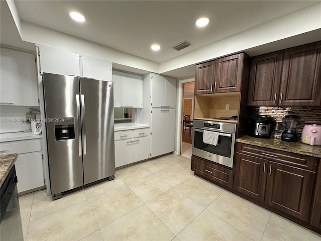 kitchen with appliances with stainless steel finishes, light stone countertops, light tile patterned floors, white cabinets, and tasteful backsplash