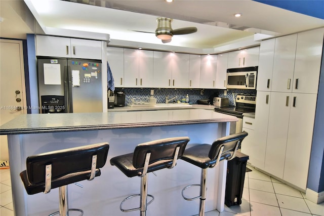 kitchen featuring light tile patterned flooring, a kitchen breakfast bar, white cabinets, and stainless steel appliances