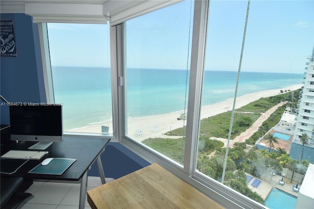 office featuring a water view, tile patterned flooring, a view of the beach, and a healthy amount of sunlight