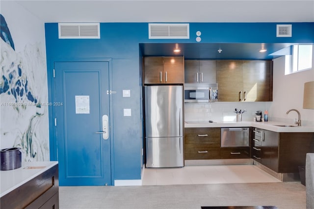 kitchen featuring tasteful backsplash, light tile patterned floors, appliances with stainless steel finishes, dark brown cabinetry, and sink