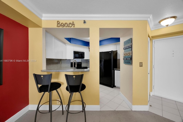 kitchen with ornamental molding, white cabinetry, black appliances, and light tile patterned floors