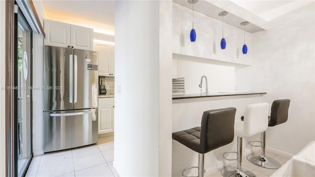 kitchen with white cabinetry, light tile patterned flooring, decorative light fixtures, and stainless steel fridge