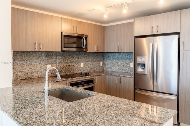 kitchen with backsplash, track lighting, sink, light stone counters, and stainless steel appliances