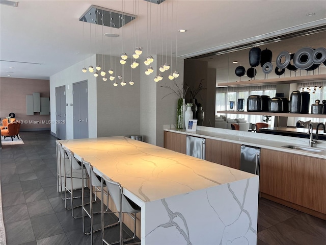 kitchen featuring decorative light fixtures, a spacious island, light stone countertops, and sink