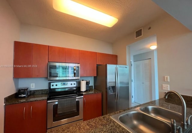 kitchen with appliances with stainless steel finishes, a textured ceiling, sink, and dark stone countertops