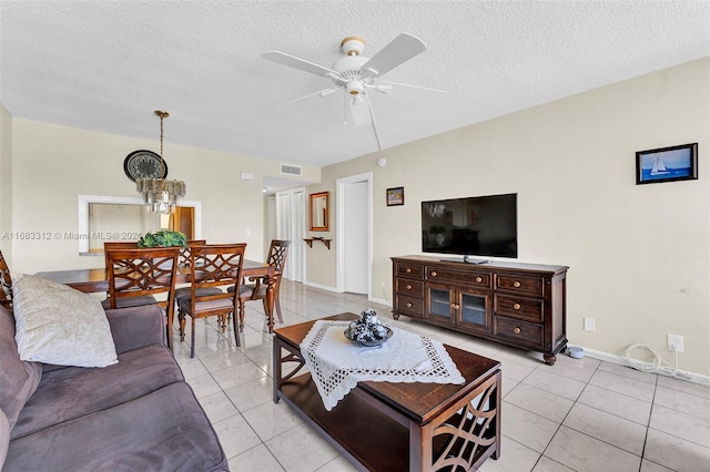 living room featuring a textured ceiling, light tile patterned flooring, and ceiling fan with notable chandelier