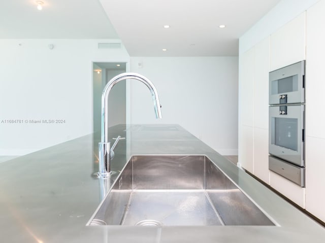 room details with white cabinetry, sink, and stainless steel counters