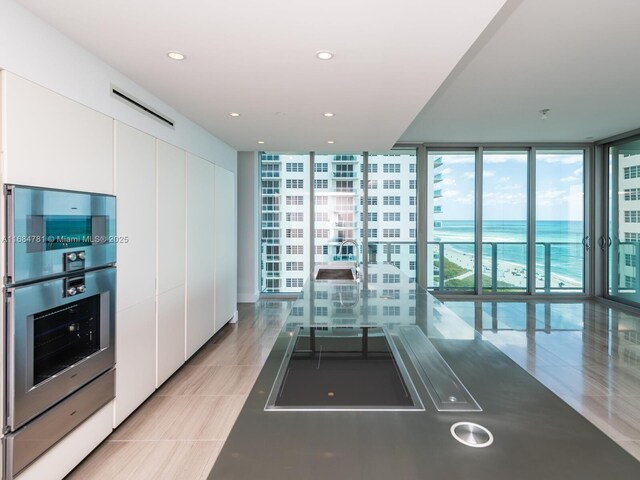 kitchen featuring expansive windows, white cabinets, black electric cooktop, and stainless steel double oven