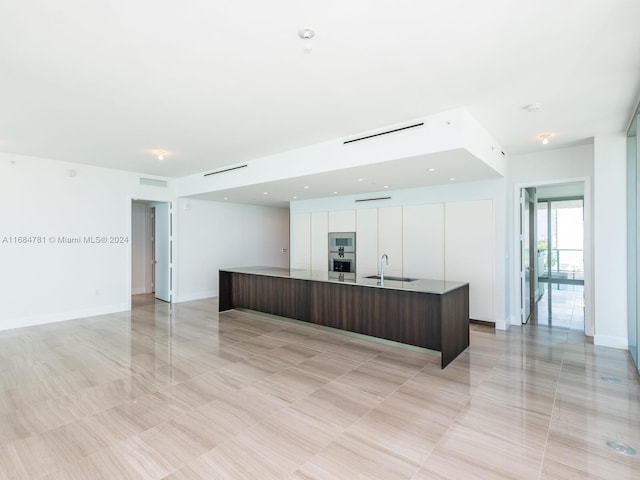 kitchen featuring white cabinets, dark brown cabinets, stainless steel microwave, a kitchen island with sink, and sink