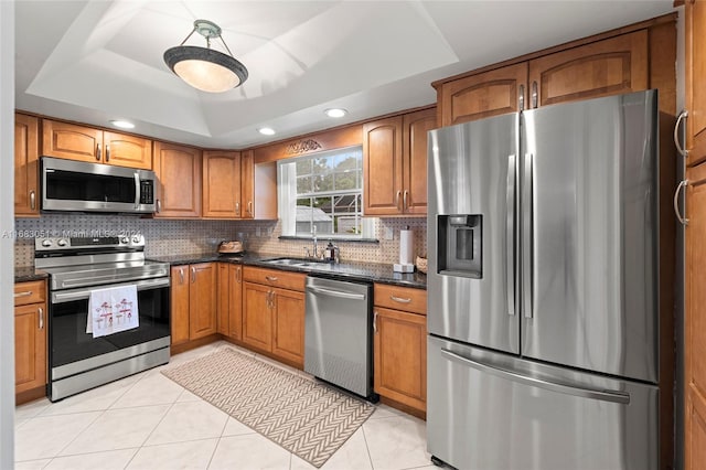 kitchen featuring a tray ceiling, stainless steel appliances, dark stone counters, decorative backsplash, and light tile patterned floors