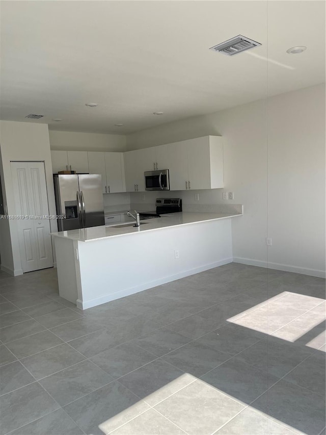 kitchen featuring kitchen peninsula, sink, white cabinets, light tile patterned floors, and appliances with stainless steel finishes