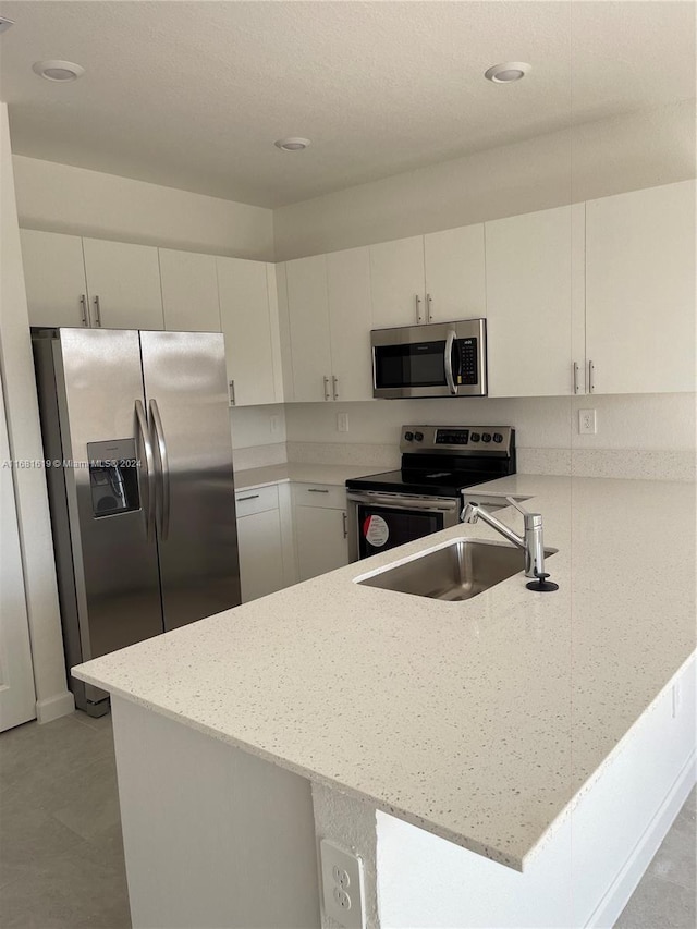 kitchen featuring stainless steel appliances, light stone countertops, a peninsula, and a sink