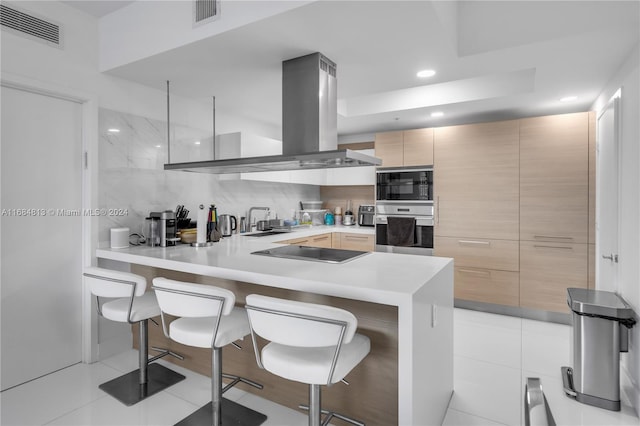 kitchen with black electric stovetop, light brown cabinetry, island range hood, kitchen peninsula, and a breakfast bar