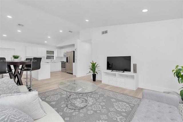 living room with light hardwood / wood-style flooring, sink, and vaulted ceiling