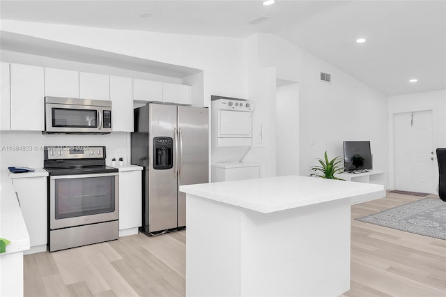 kitchen with lofted ceiling, white cabinets, appliances with stainless steel finishes, a center island, and stacked washer and clothes dryer