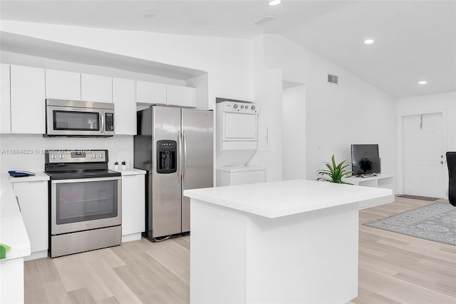 kitchen with appliances with stainless steel finishes, stacked washer / drying machine, light wood finished floors, and lofted ceiling