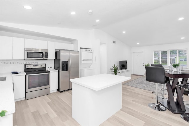 kitchen featuring stacked washer and dryer, appliances with stainless steel finishes, vaulted ceiling, light countertops, and white cabinetry