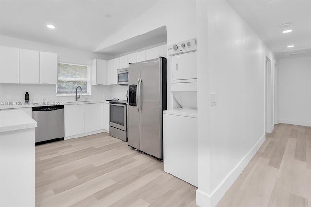 kitchen with white cabinets, light wood-type flooring, stacked washer and dryer, sink, and stainless steel appliances