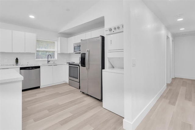 kitchen with stacked washer / drying machine, appliances with stainless steel finishes, a sink, and light wood-style flooring