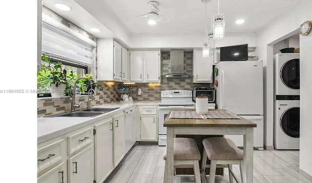 kitchen with white cabinetry, stacked washer / drying machine, wall chimney exhaust hood, sink, and white appliances