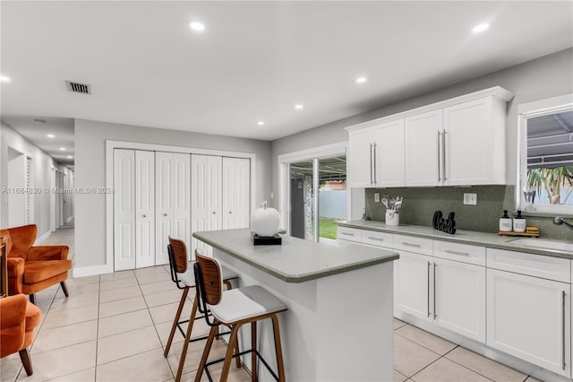 kitchen featuring white cabinets, light tile patterned floors, a kitchen island, backsplash, and sink