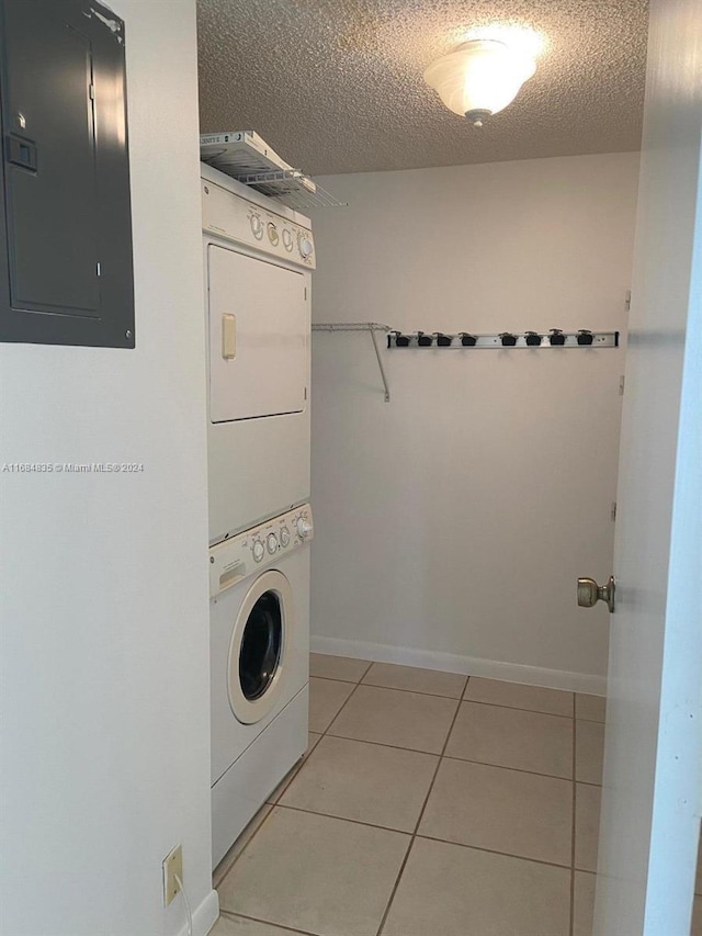 clothes washing area with stacked washer / drying machine, electric panel, a textured ceiling, and light tile patterned floors