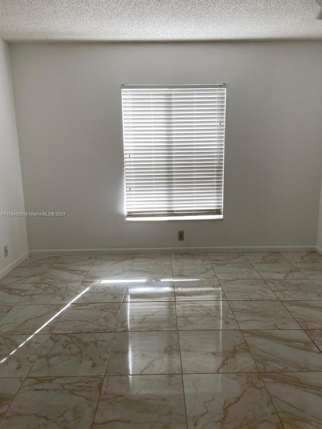 814 Sky Pine Way Unit C1, Green Acres, FL 33415 - empty room with marble look tiles, a textured ceiling, and baseboards