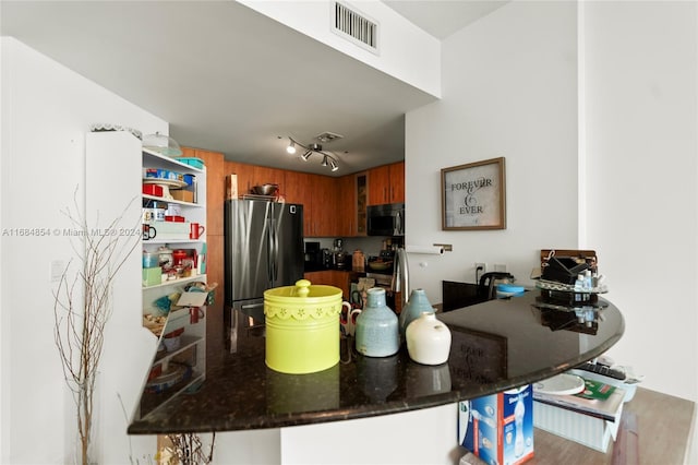 kitchen with kitchen peninsula, rail lighting, stainless steel appliances, dark stone counters, and a breakfast bar area