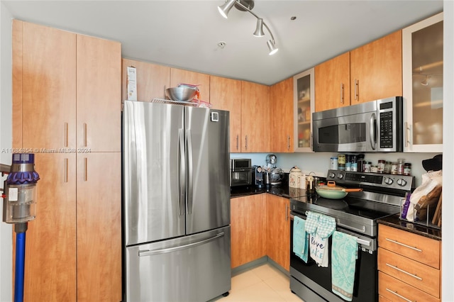 kitchen featuring rail lighting, stainless steel appliances, dark stone counters, and light tile patterned flooring