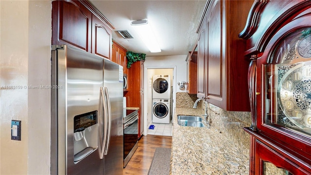 kitchen featuring tasteful backsplash, sink, stacked washer / dryer, light stone countertops, and stainless steel appliances