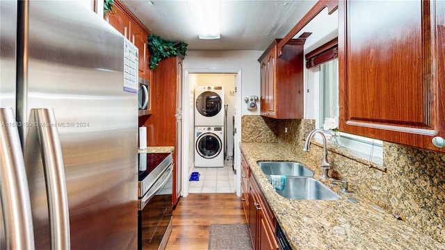 kitchen with stacked washer and dryer, appliances with stainless steel finishes, decorative backsplash, light stone counters, and sink