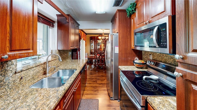 kitchen featuring appliances with stainless steel finishes, backsplash, light stone countertops, a chandelier, and sink