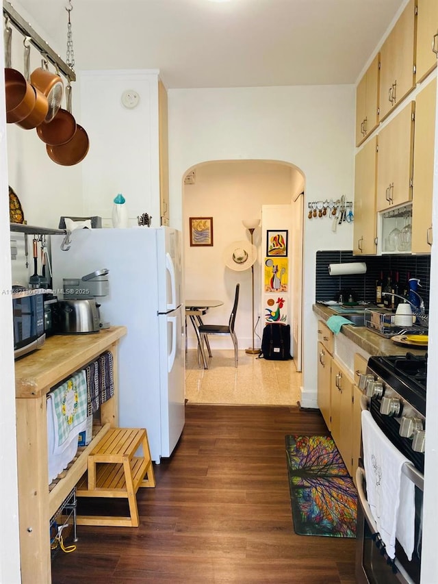 kitchen featuring arched walkways, dark wood-style flooring, range with gas stovetop, decorative backsplash, and stainless steel microwave